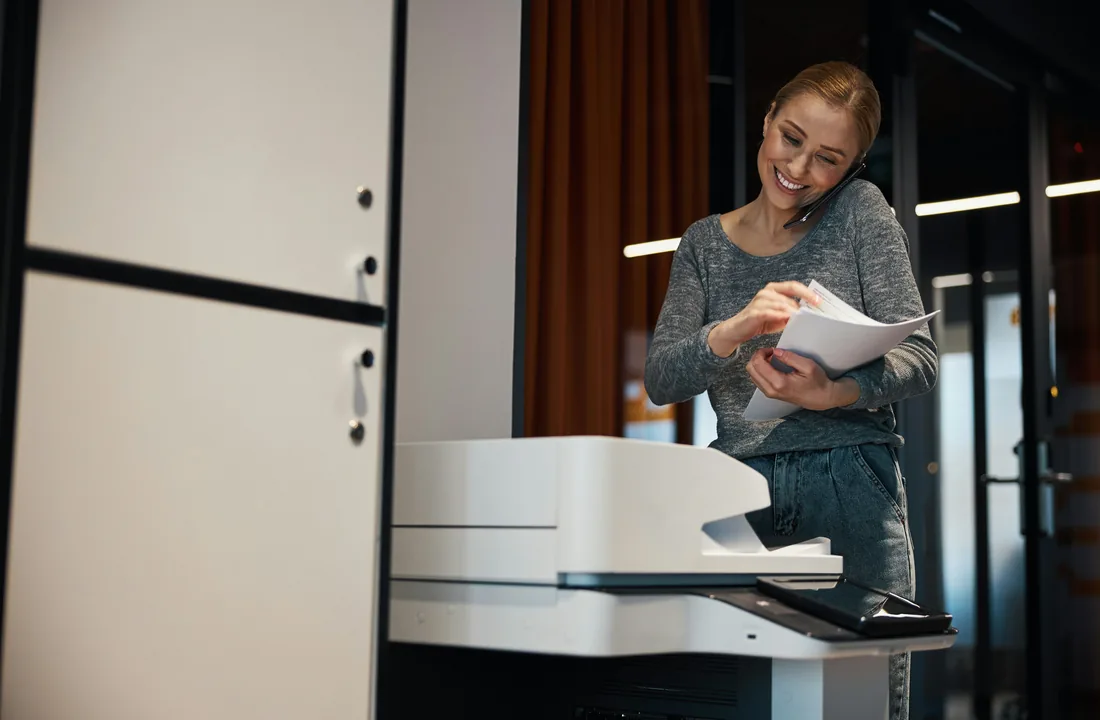 Office worker holding documents beside a photocopier